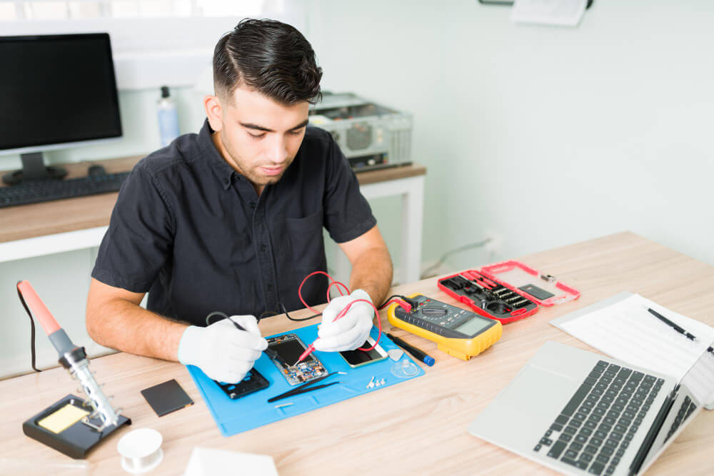 hispanic-male-engineer-checking-connections-damaged-smartphone-with-multimeter-his-repair-shop